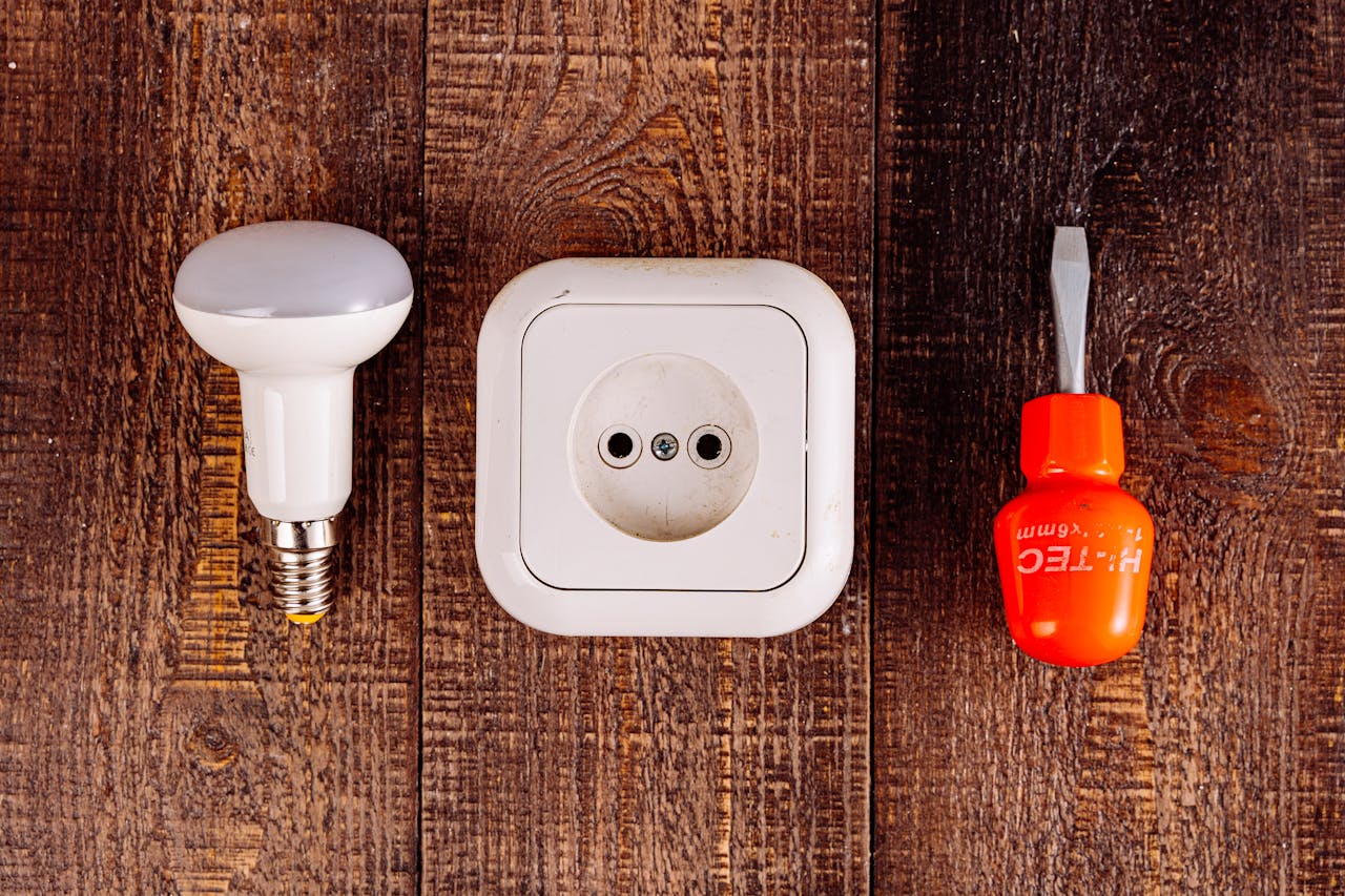 Flat lay of a lightbulb, socket, and screwdriver on a rustic wooden surface.