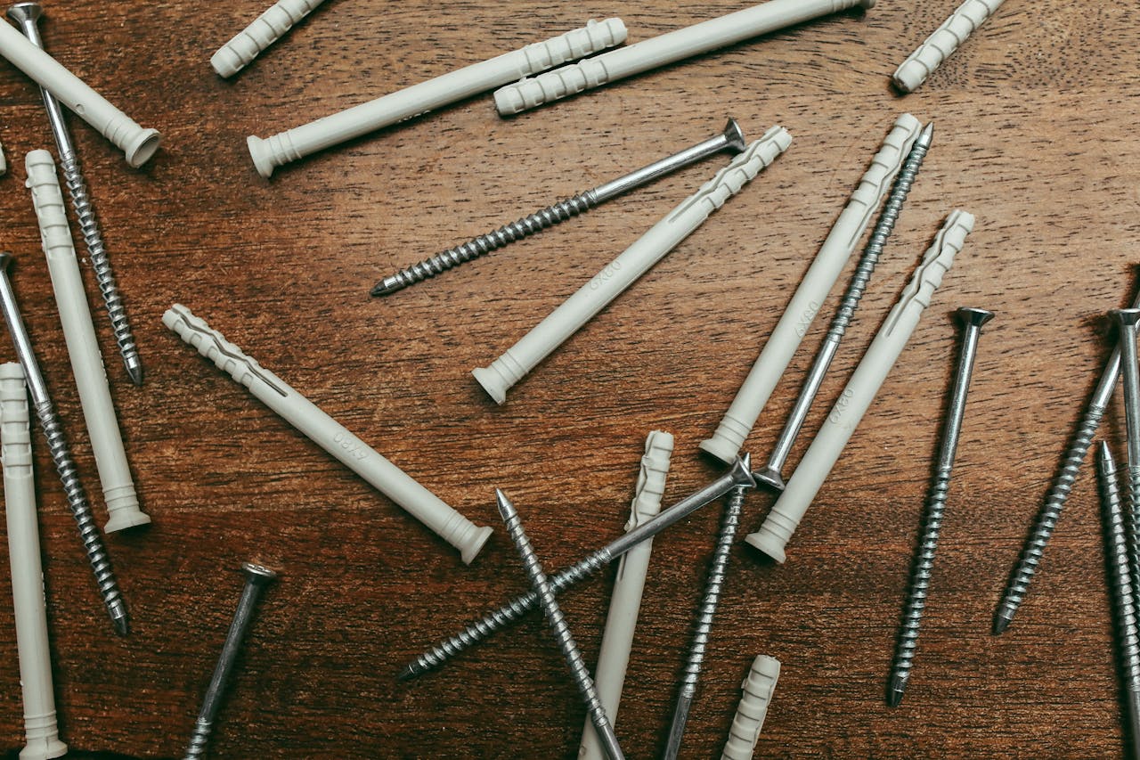High-angle view of metal screws and plastic wall plugs on a wooden surface.