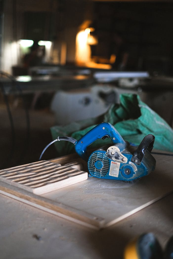 Blue electrical special tool for wood polishing placed on workbench with wooden board in professional joinery with equipment on blurred background
